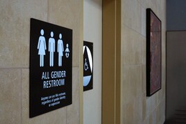 Un cartello 'tutti i generi' davanti ad un bagno in un aeroporto